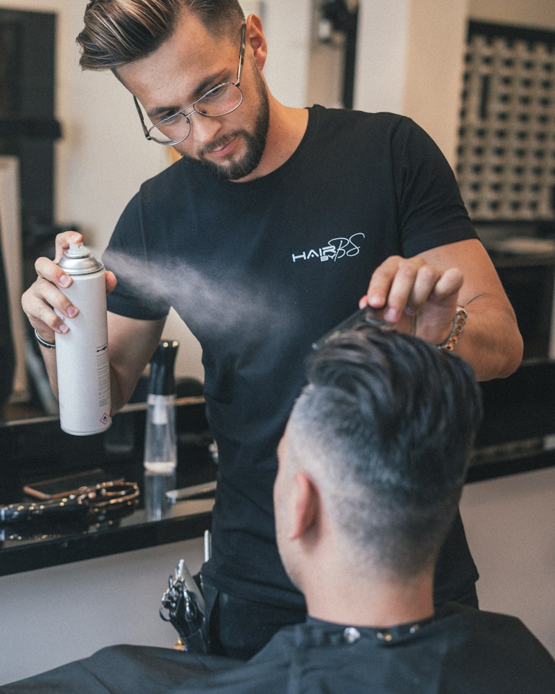 Barber in a black shirt misting a guest’s hair before styling.