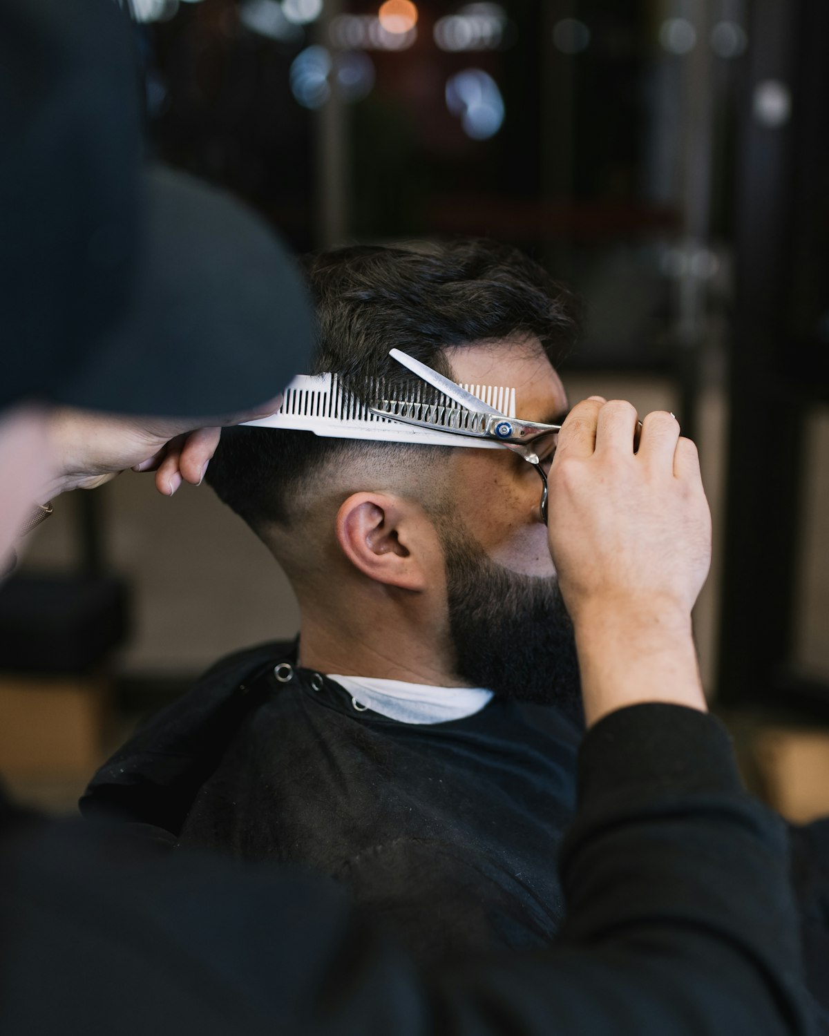 Close view of scissors cutting hair beside a barber’s hands.